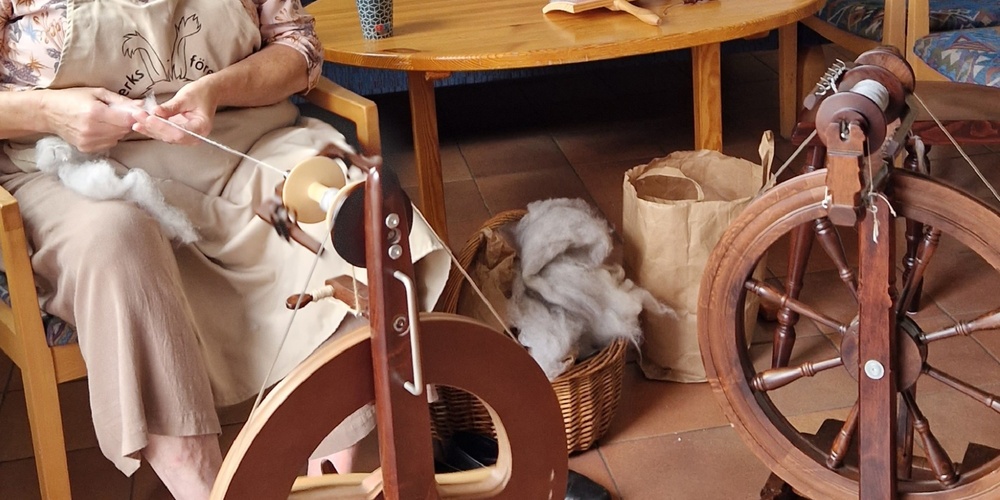 En person spinner garn med en spinnrock i ett vardagsrum med soffor och bord.