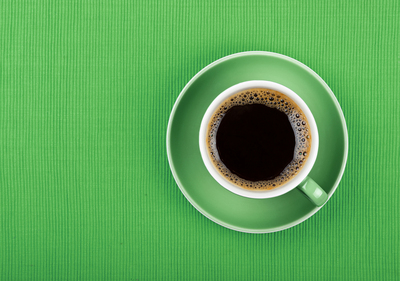 En kopp svart kaffe i en grön kopp och fat, sedd uppifrån på en grön bakgrund.