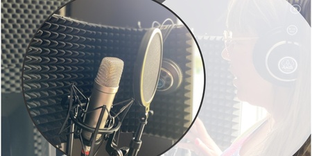 En person med hörlurar spelar in röst i en ljudstudio med mikrofon och popfilter.