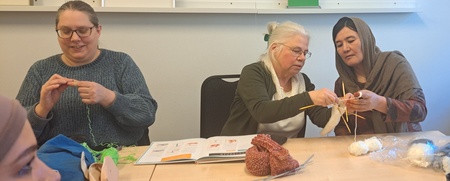 Fyra kvinnor sitter runt ett bord och stickar tillsammans i ett ljust rum.