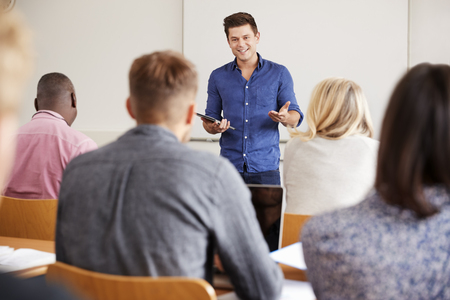 En man står framför en grupp och håller en presentation i ett klassrum.