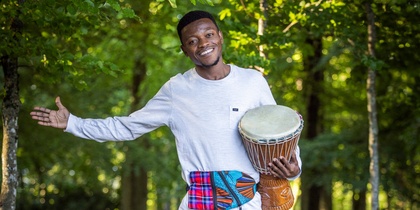 En leende man står barfota på en trästig i skogen och håller en trumma under armen.