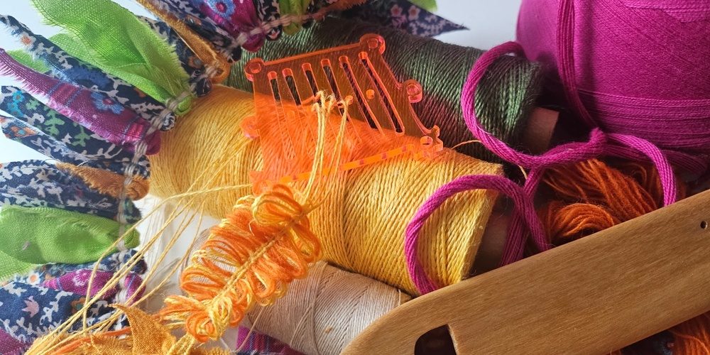 Närbild av färgglada sytrådar, garn, tygbitar och ett vävverktyg på ett bord.