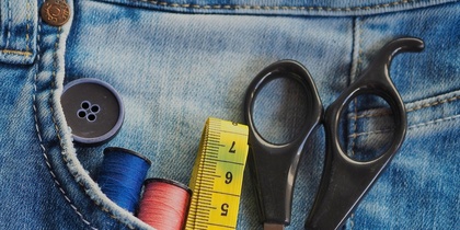 Knapp, måttband, tråd och sax instucket i en bakficka på ett par jeans.