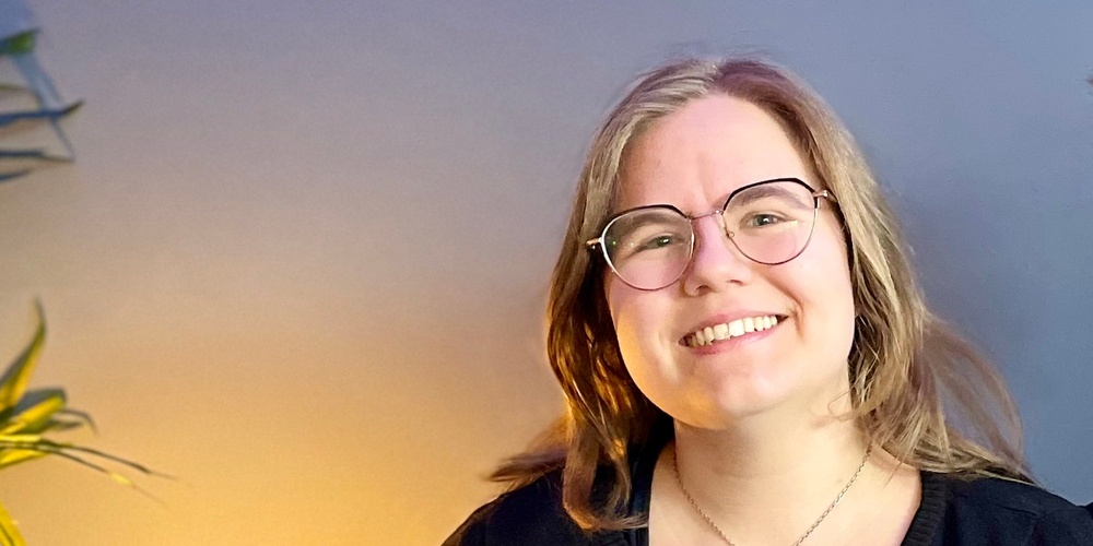 Två leende personer sitter tillsammans i en blå soffa i ett rum med blå vägg och grön växt.