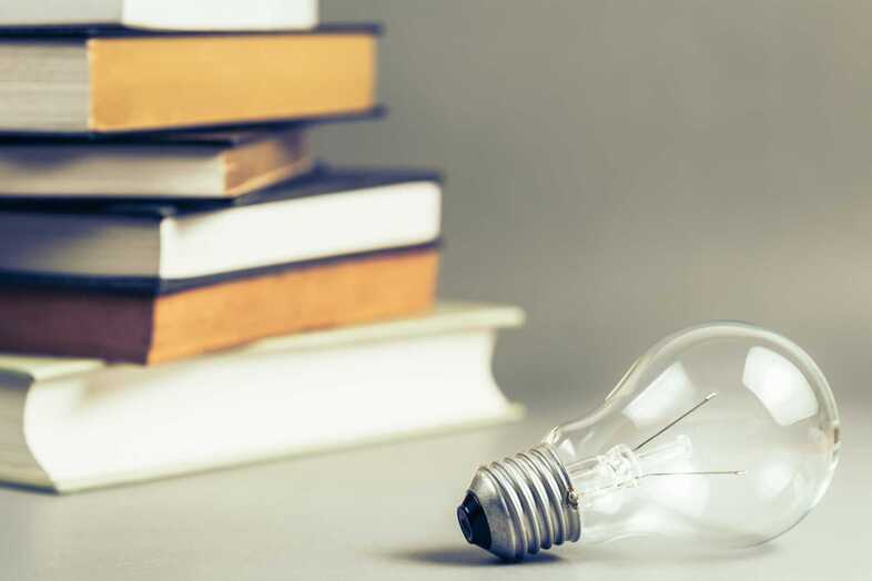 En glödlampa som ligger framför en trave böcker.