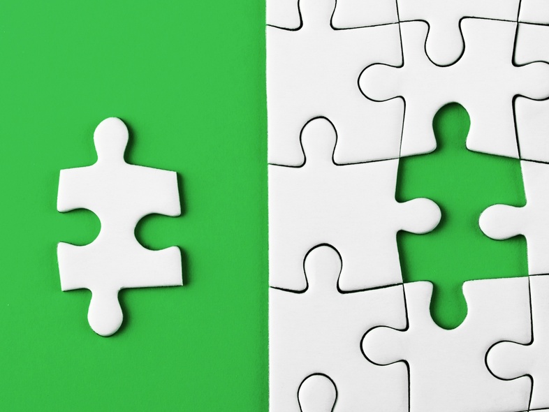 En pusselbit ligger bredvid ett pussel med en tom plats på en grön bakgrund.