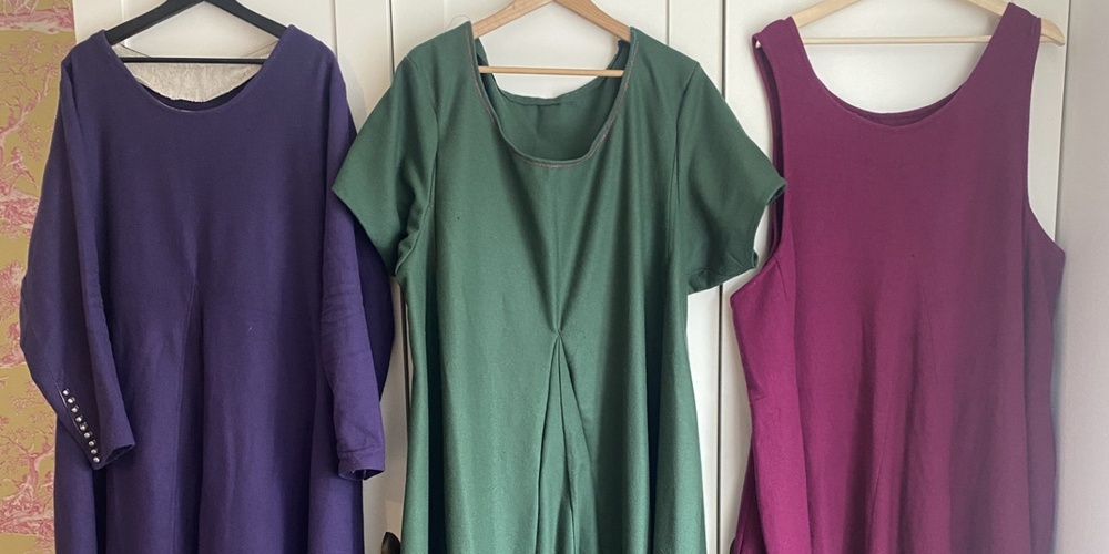 Tre långklänningar i lila, grön och vinröd hänger på galgar framför en vit garderob.