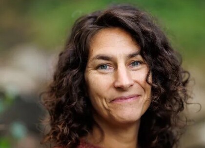 Person med mörkt, lockigt hår utomhus med grön bakgrund.