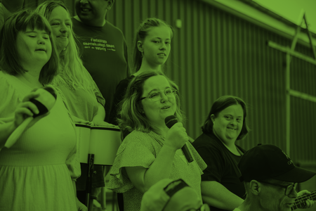 En grupp människor, varav en kvinna håller en mikrofon, sitter tillsammans inomhus. Bilden har grön färgton.