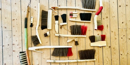 Flera olika borstar med trähandtag ligger utspridda på ett ljust trägolv.