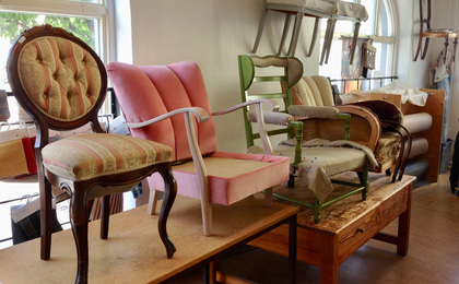 Fyra olika stolar i olika stadier av renovering står på ett bord i en ljus verkstad.