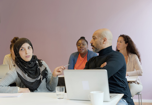 Fyra personer sitter vid ett bord i ett mötesrum och diskuterar, med en laptop och anteckningar framför sig.