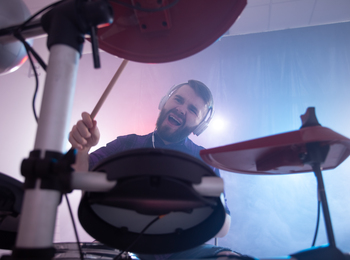 Man spelar trummor med hörlurar i en rökfylld studio, sedd underifrån.