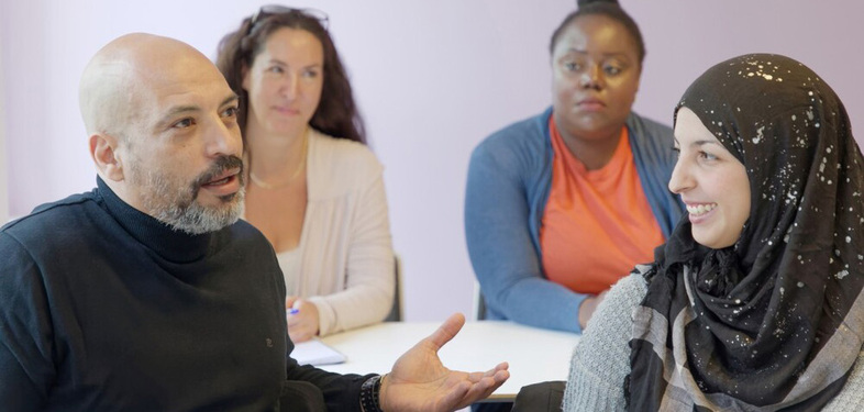 Fyra personer sitter runt ett bord och samtalar, två kvinnor och två män, i en ljus inomhusmiljö.
