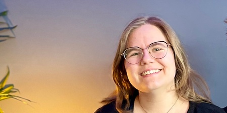 Två leende personer sitter tillsammans i en blå soffa i ett rum med blå vägg och grön växt.