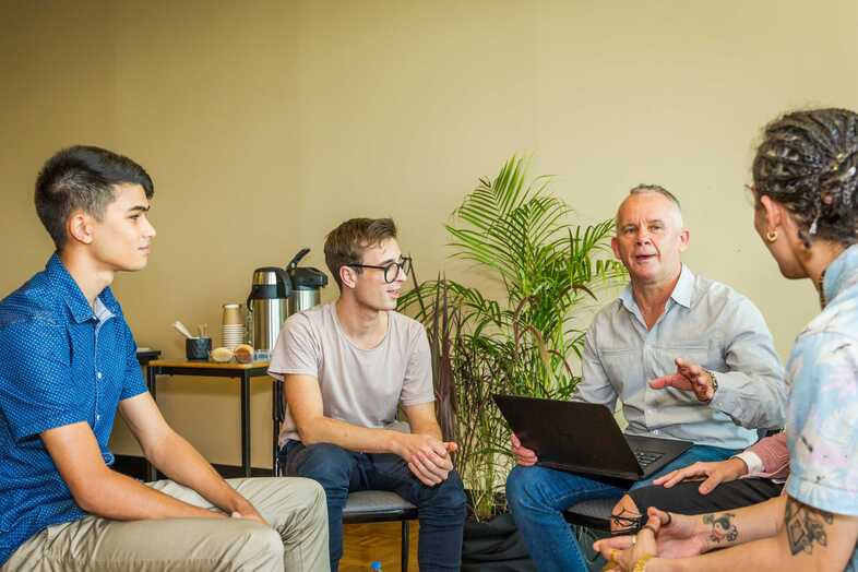 Fyra personer sitter i en ring och diskuterar. En person har en laptop i knät.