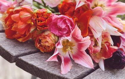 En bukett färgglada blommor ligger på ett träbord utomhus.