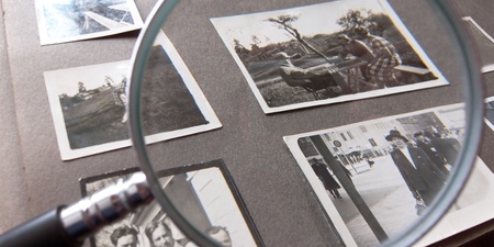 Ett fotoalbum med gamla svartvita fotografier och ett förstoringsglas ovanpå.