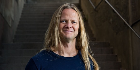 Person med långt blont hår står framför en trappa i en mörk miljö.