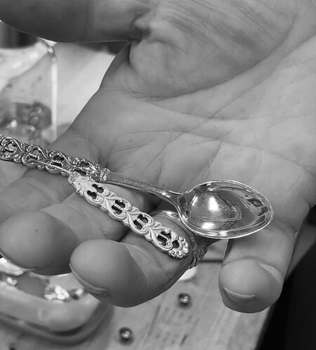 En hand håller en liten dekorerad silversked ovanför ett bord.