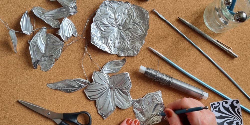 En person arbetar med metallprägling och formar blommor och blad av tunn metall på en korkmatta.