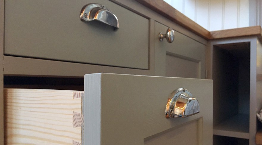 Närbild på gröna kökslådor och skåp med silverfärgade handtag, en låda är utdragen.