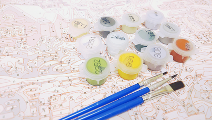 Färglådor och penslar ligger på en målarbok med numrerade fält för paint by numbers.