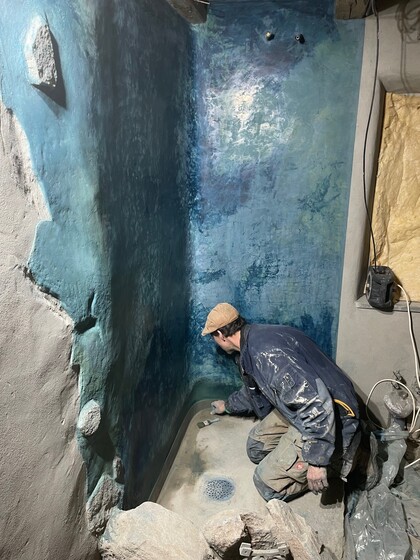 En person målar eller behandlar en duschvägg med blå nyanser i ett rum under renovering.