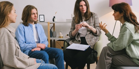 Fyra personer sitter i en cirkel och samtalar i ett ljust rum, en av dem antecknar på ett block.