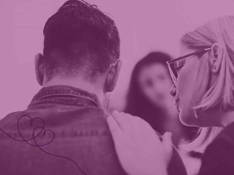 En person lägger en hand på en annans axel i en stödjande gest, med en tredje person i bakgrunden.