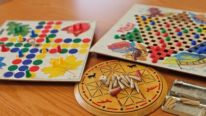 Tre olika brädspel med färgglada spelpjäser och tärning på ett träbord.