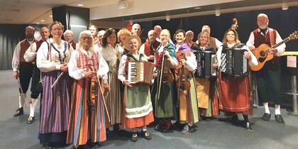 En grupp människor i folkdräkter spelar traditionella instrument inomhus.