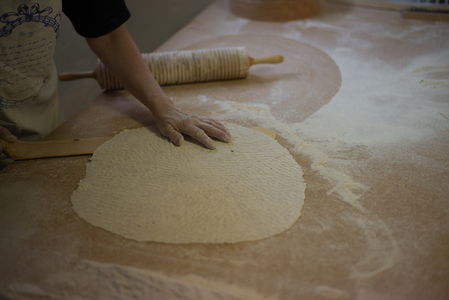 En person kavlar ut en stor, tunn deg på ett mjölat bord med en kruskavel.