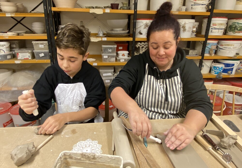 En pojke och en kvinna arbetar med lera vid ett bord i en keramikverkstad.