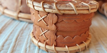 Liten rund ask av björknäver med dekorativa sömmar, placerad på ett ljust tygunderlag.