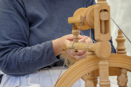 Person spinner garn med en gammaldags spinnrock, fokus på händer och verktyg.