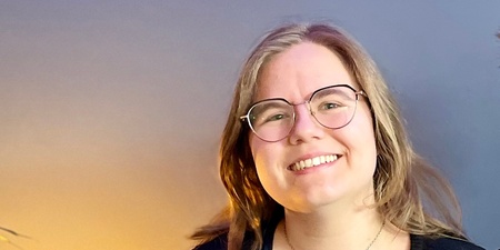 Två leende personer sitter tillsammans i en blå soffa i ett rum med blå vägg och grön växt.