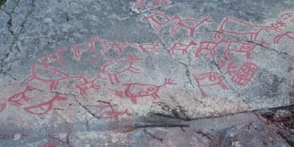Hällristningar med röda figurer av djur och människor på en stenhäll utomhus.