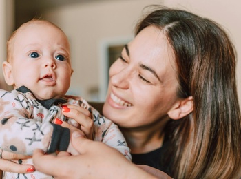 En mamma håller upp sin bäbis, två armar till från en andra förälder syns i förgrunden.