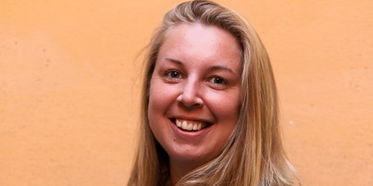Leende kvinna med långt blont hår framför en orange vägg.