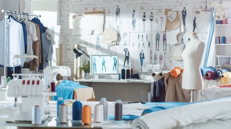 Ett kreativt modeateljé med symaskiner, tyg, provdocka och skisser på väggen.