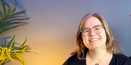 Två leende personer sitter tillsammans i en blå soffa i ett rum med blå vägg och grön växt.