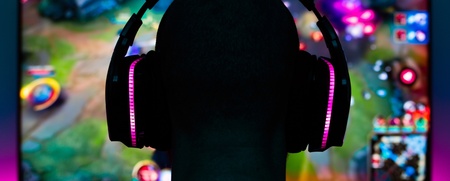 En person med hörlurar sitter framför en datorskärm och spelar ett färgglatt datorspel.