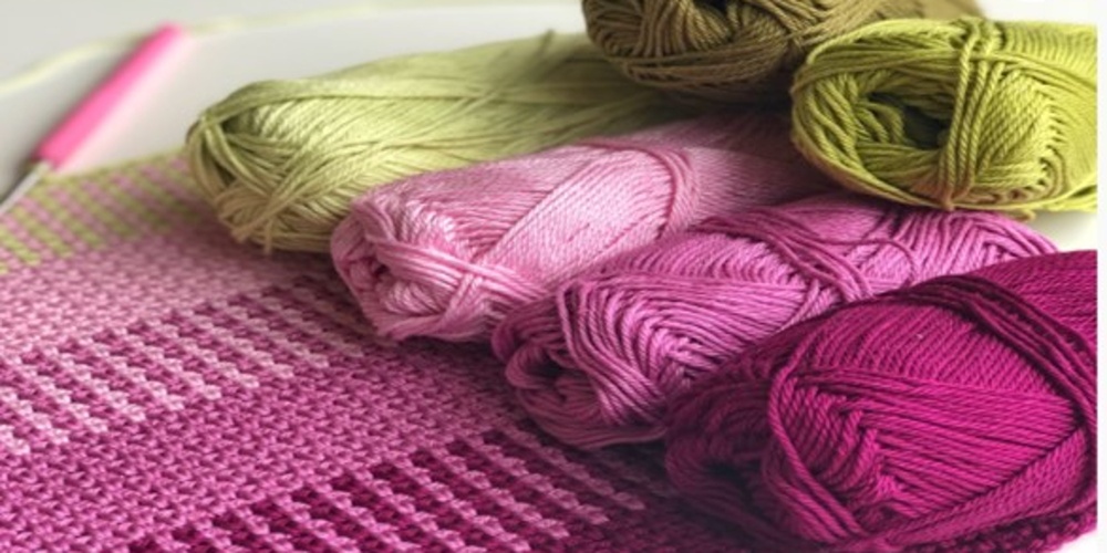 Flera garnnystan i rosa och gröna nyanser ligger på ett stickat tyg med liknande färger.