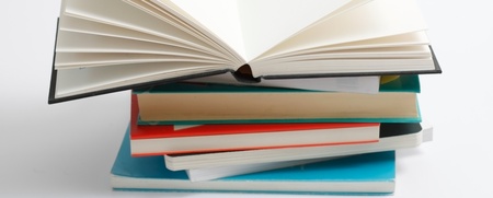 En hög med böcker där den översta boken är uppslagen och resten är stängda, mot vit bakgrund.