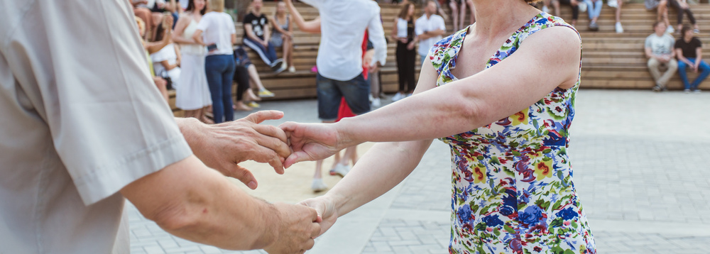 Två personer dansar tillsammans utomhus, med publik sittande i bakgrunden.
