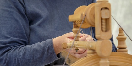 Person spinner garn med en gammaldags spinnrock, fokus på händer och verktyg.