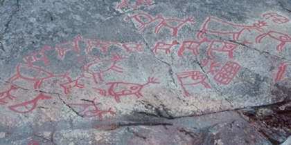 Hällristningar med röda figurer av djur och människor på en stenhäll utomhus.