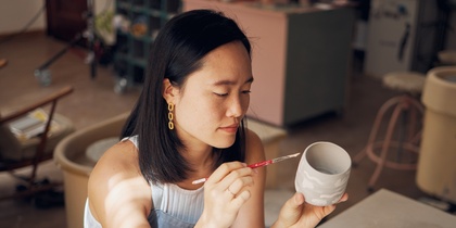 En kvinna målar en keramikmugg med pensel i en ljus keramikstudio.